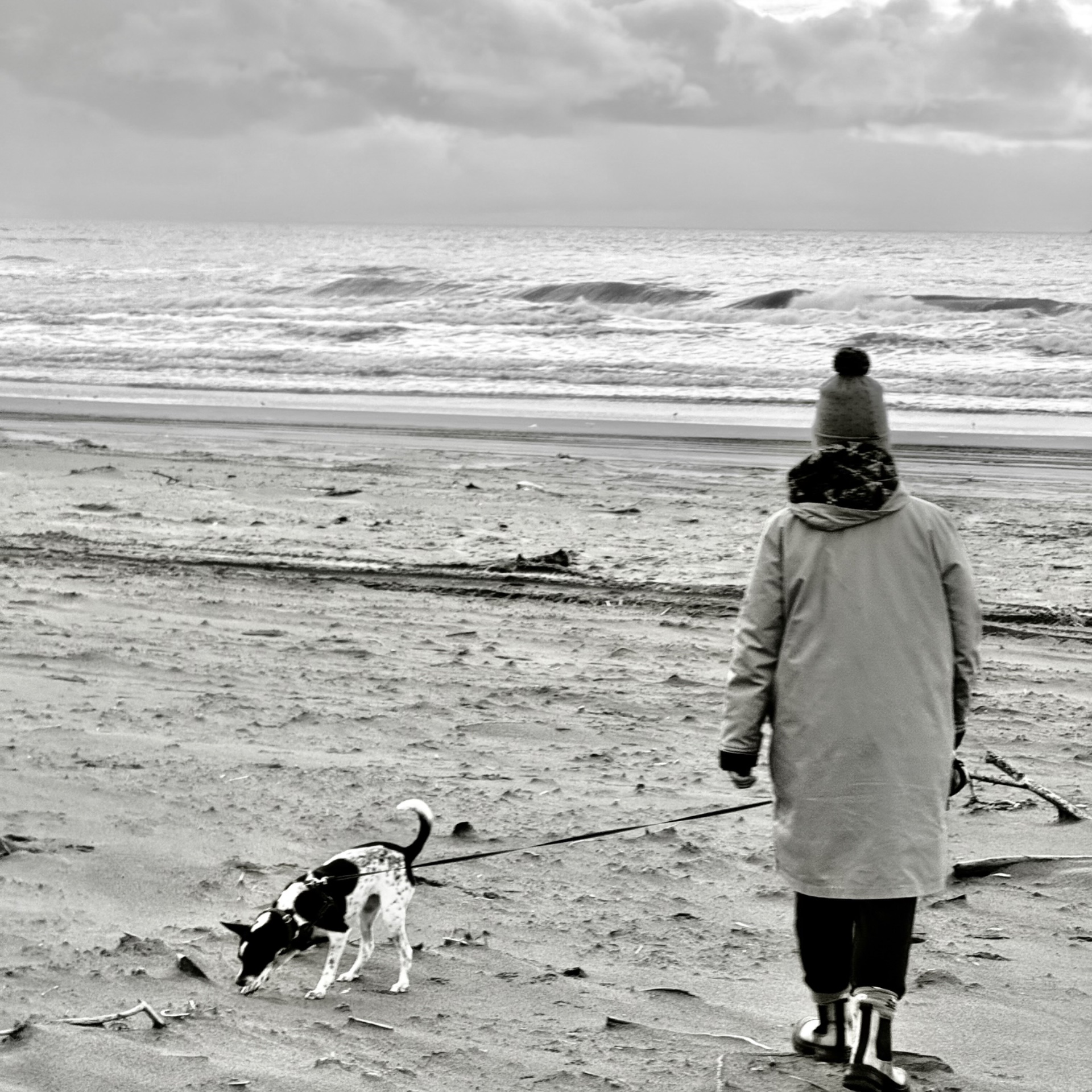 A walk along the beach with a dog as the surf rolls in, in black and white